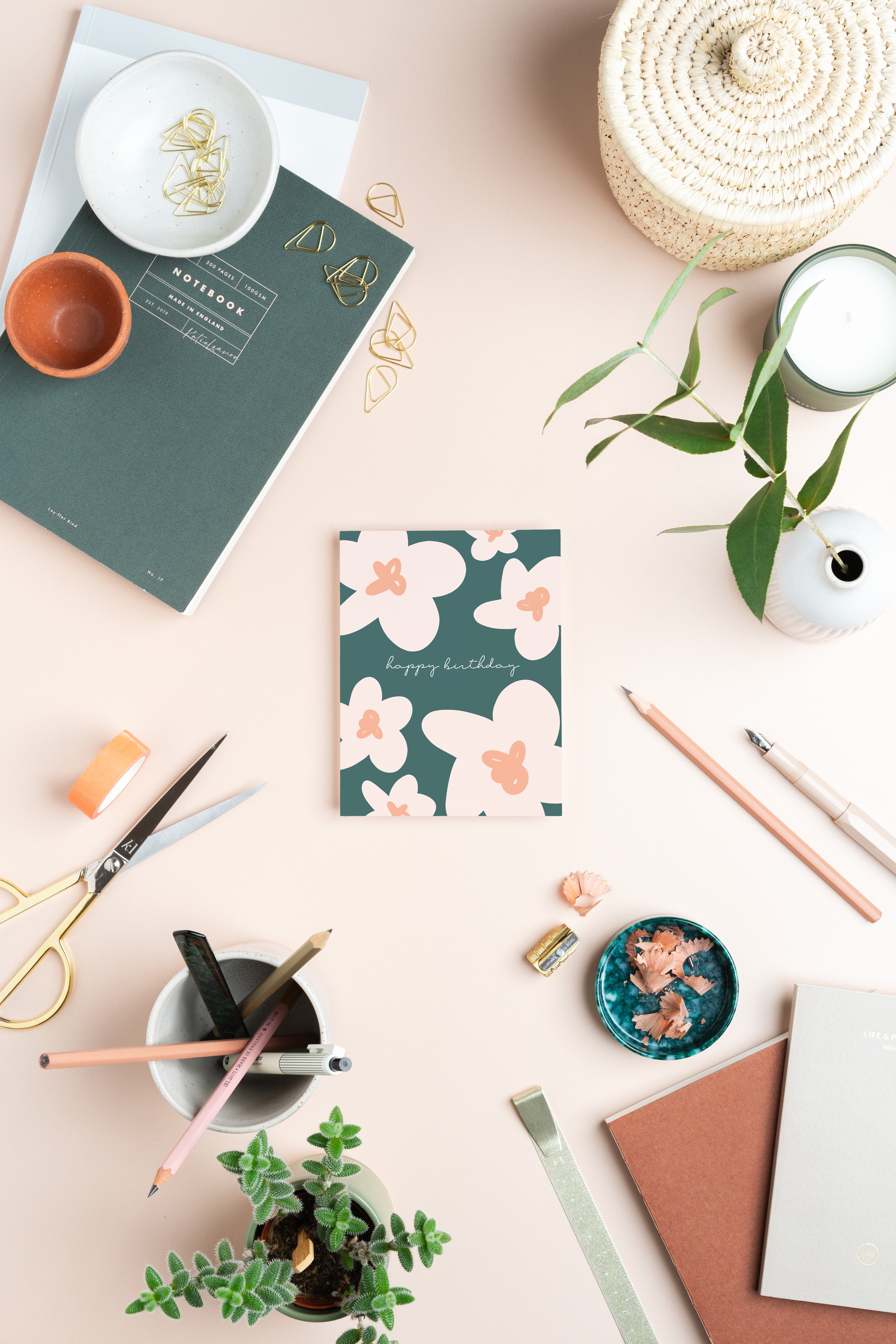 Desk setup with stationery items including a notebook, pens, and a small plant on a light background.