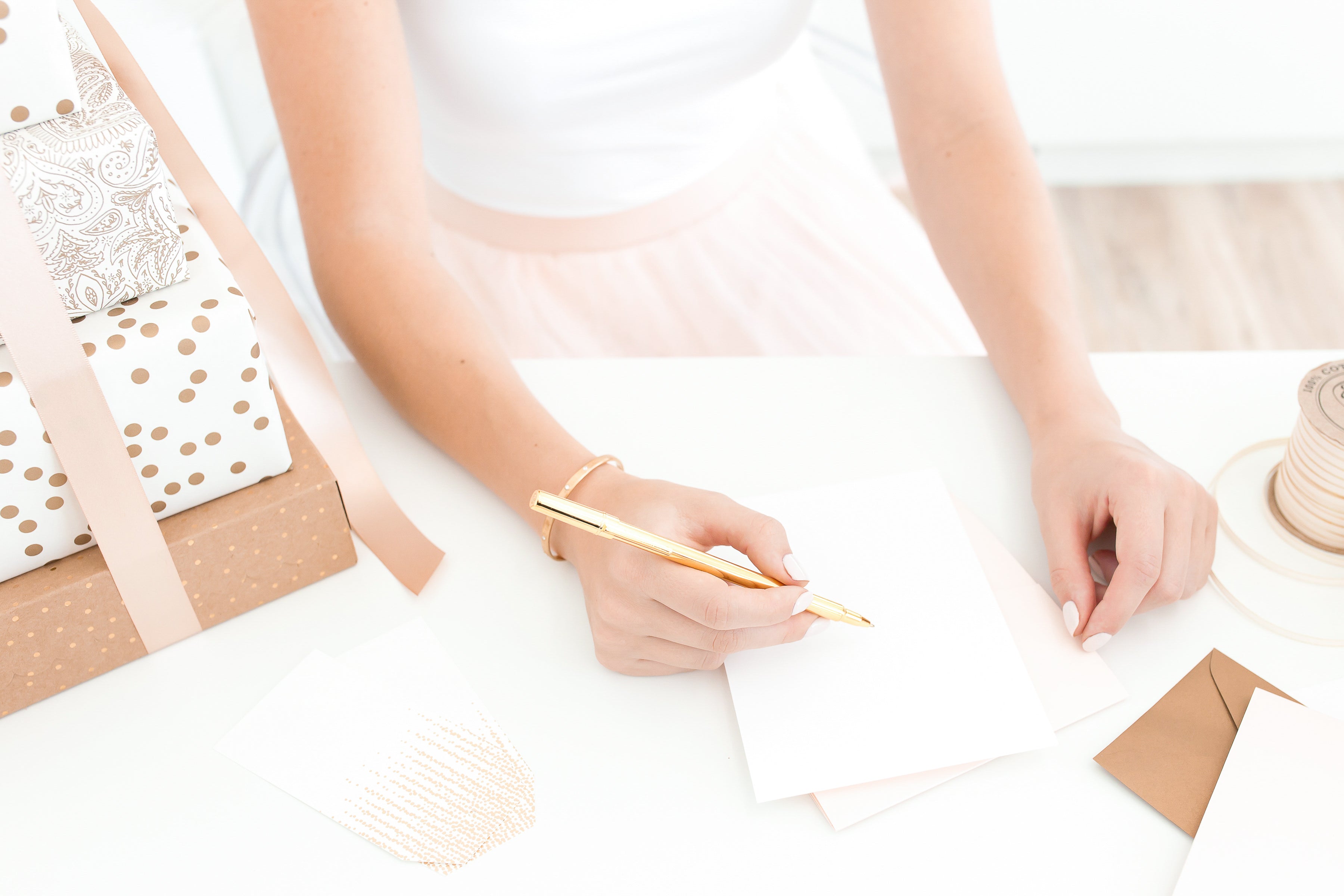 Person writing on a piece of paper with a pen, surrounded by gift-wrapping materials.